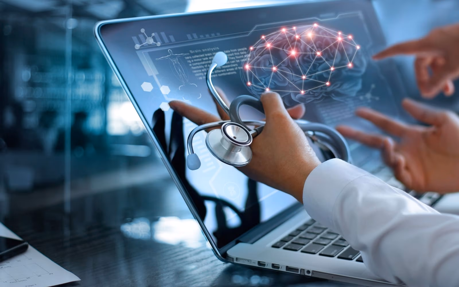 A clinician's hand holding a stethoscope in front of a laptop showing a medical analysis screen.